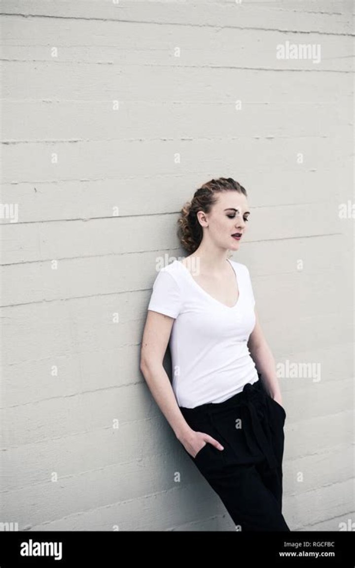 a woman leaning against a wall with her hands on her hips and looking