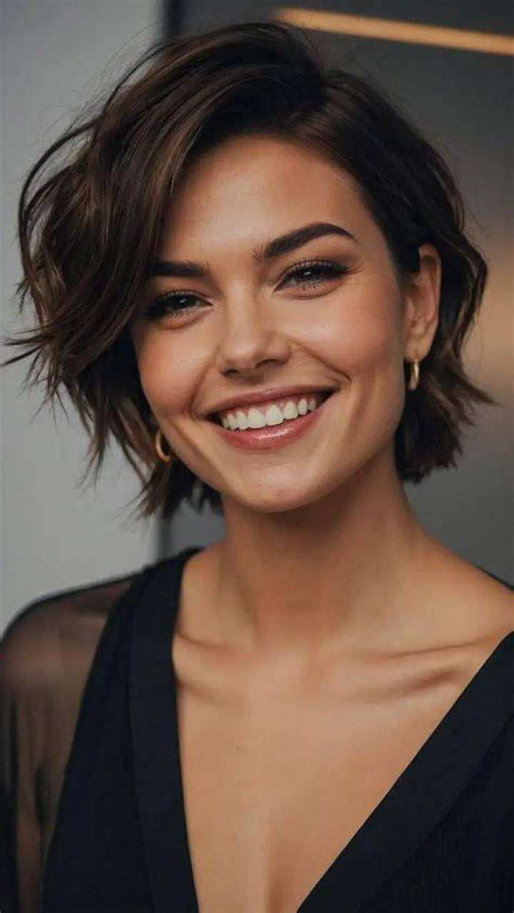 a woman with short hair standing in front of a white wall wearing a